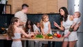 A young family with many children cooks together in the kitchen. Mom teaches her daughters how to cook.