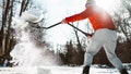 Mature man clearing up snow on outdoor ice skating rink. Exterior of frozen pond in public park.