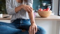 Close-up of young woman scratching her arm while sitting on the stool in the home kitchen.