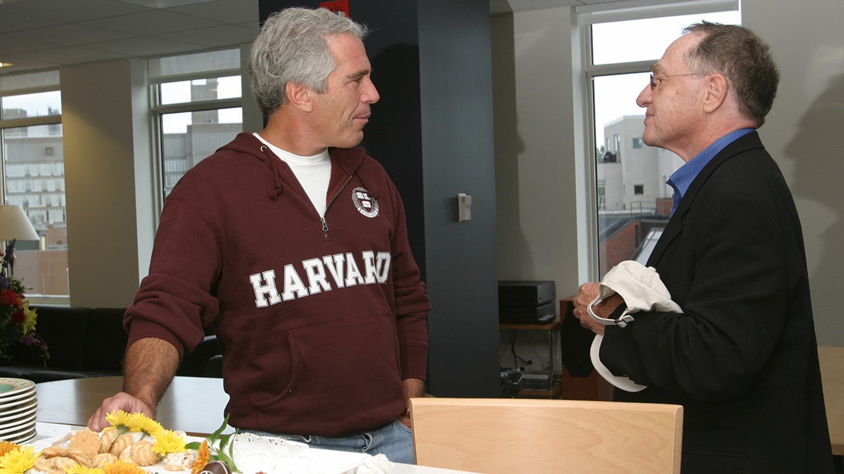 Jeffrey Epstein talks with Alan Dershowitz in front of a table with food
