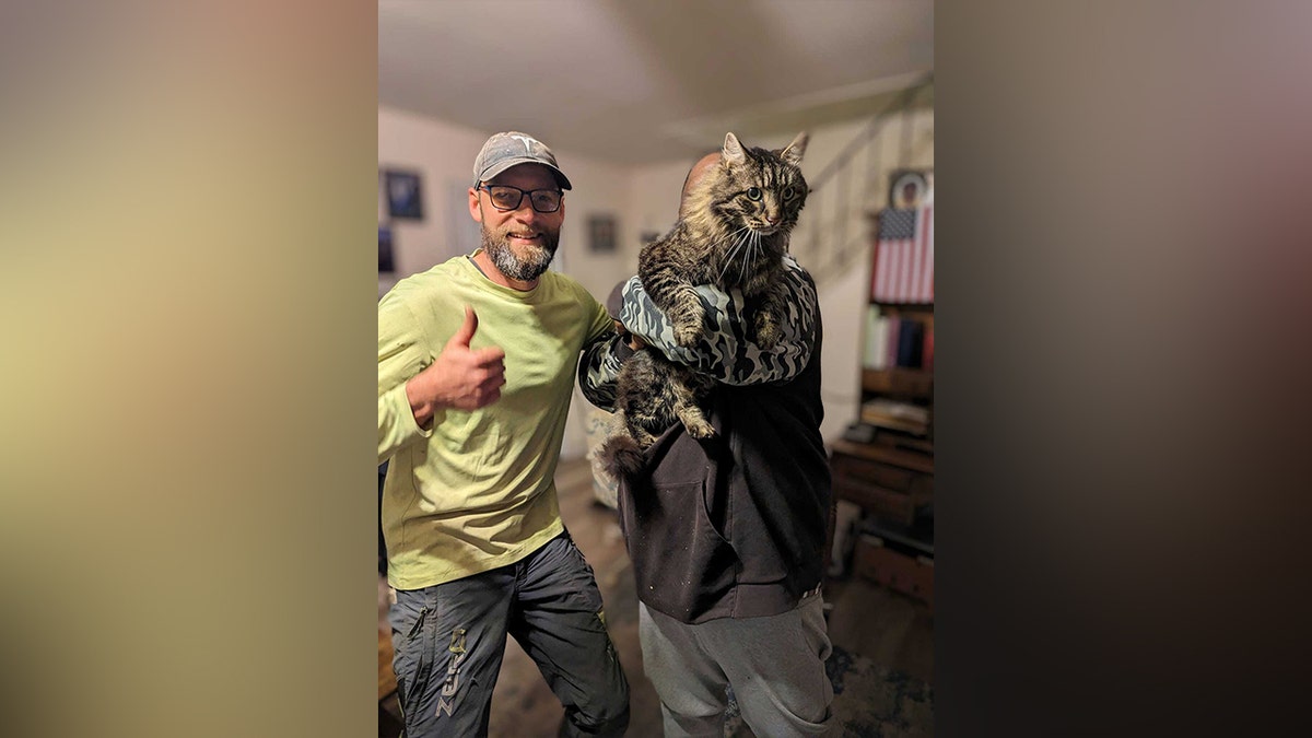 Murrow making a thumbs-up gesture next to owner holding cat