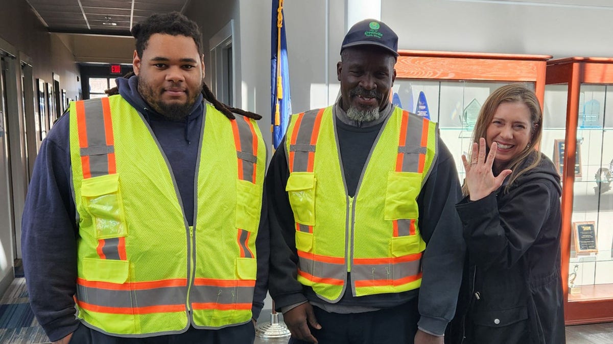 two men in hi-vis smiling with woman showing ring