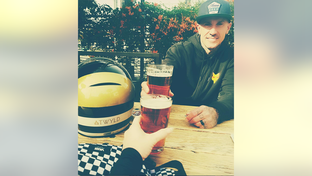 Carey Hart smiles holding a glass of beer cheersing Pink