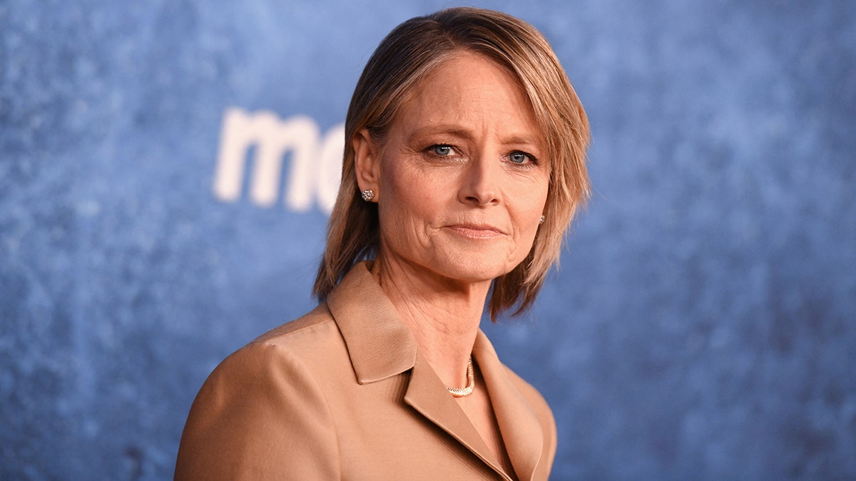 Jodie Foster in a sand colored jacket looks serious on the carpet