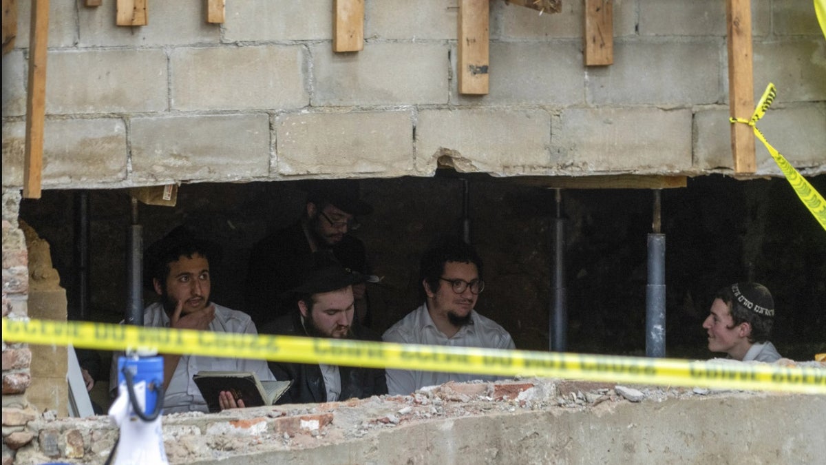 Jewish students sit behind a breach in the wall of a synagogue that led to a tunnel dug by the students in New York.