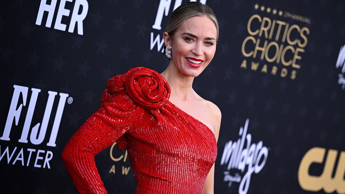 Emily Blunt em um vestido vermelho brilhante com rosas no ombro no tapete do Critics Choice Awards
