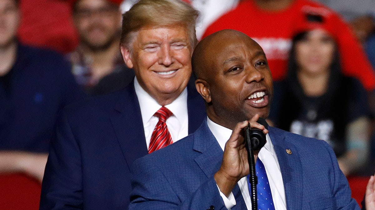 Tim Scott speaks on stage with Trump behind him