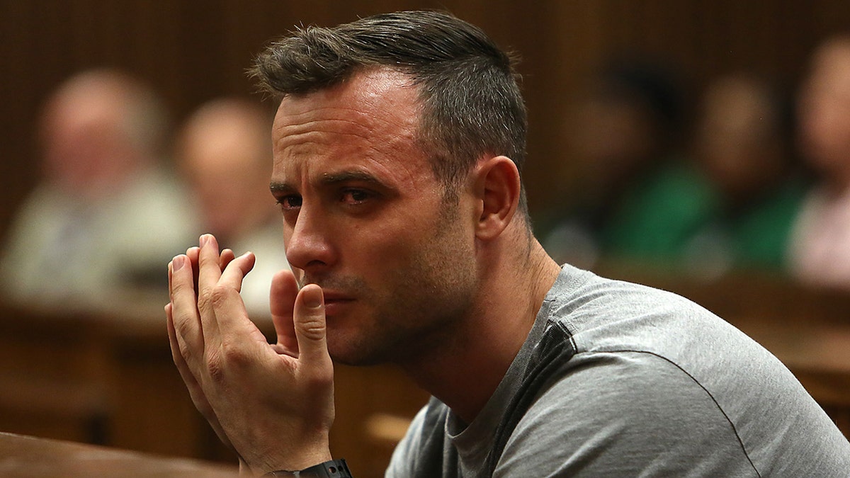 Blade Runner Oscar Pistorius crying in court, red eyes, hands held in front of his mouth, wearing a grey shirt