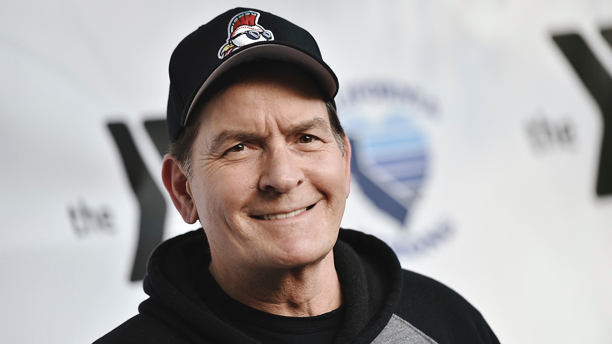 Close up of Charlie Sheen smiling wearing a baseball hat