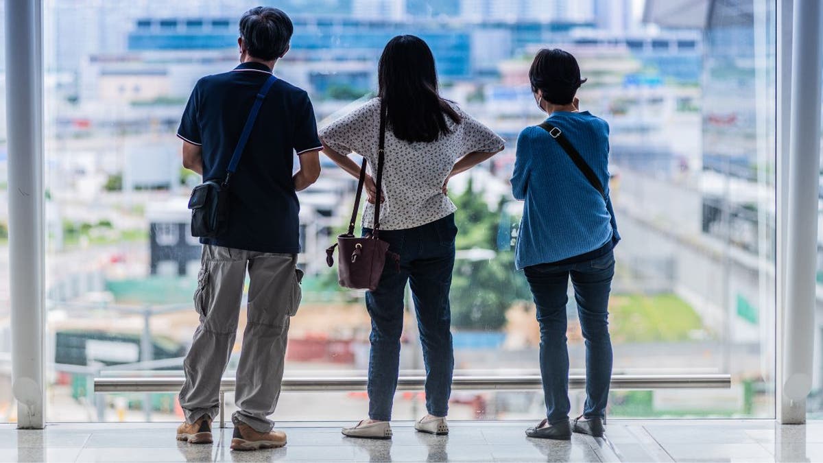 Three people look out a window at an airport