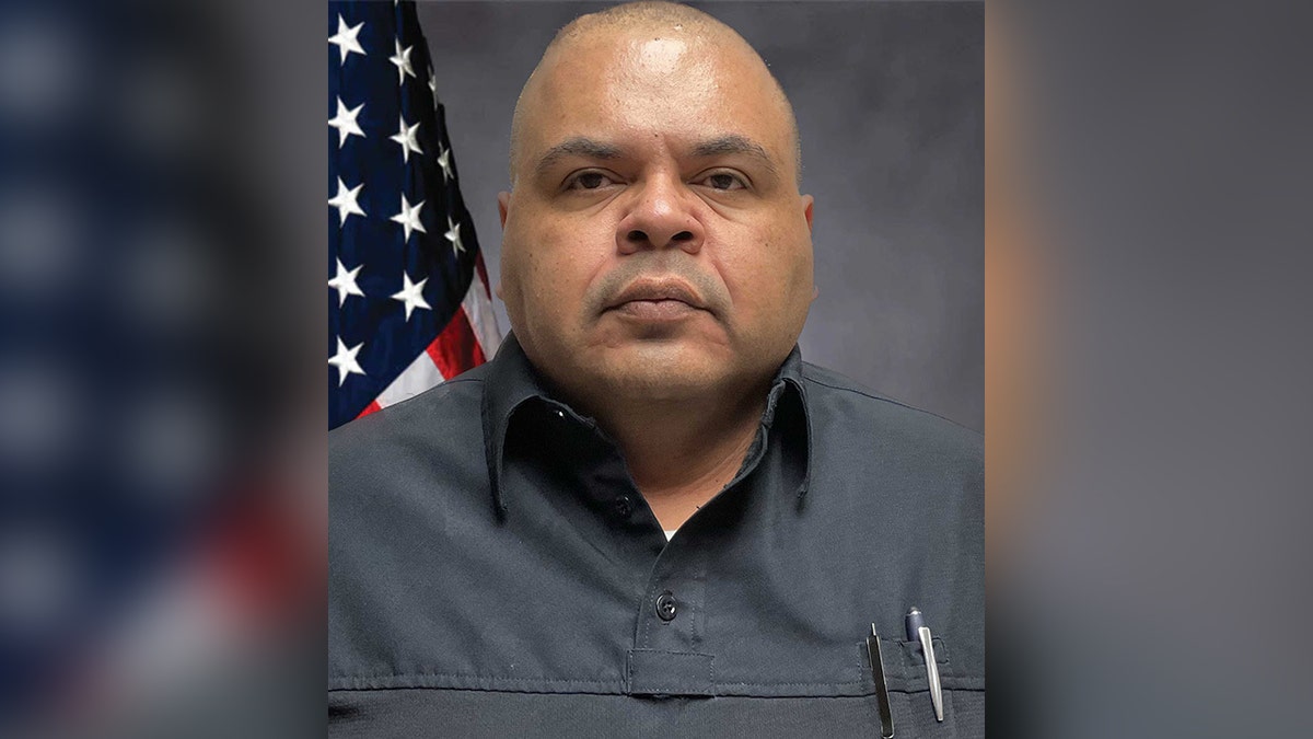 Deputy Mendoza in dark gray shirt, American flag behind him