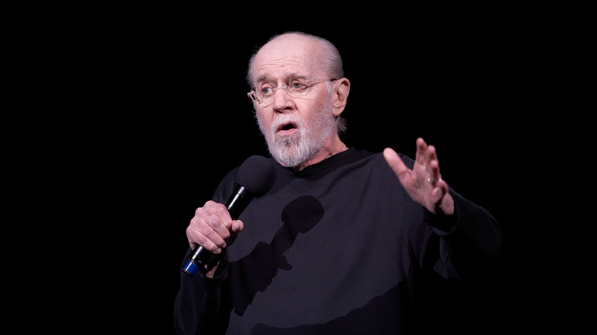 George Carlin no palco com um microfone