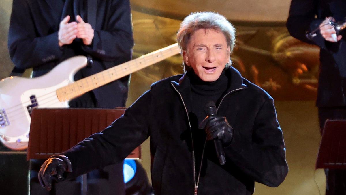 barry manilow holding a micriphone and smiling on stage