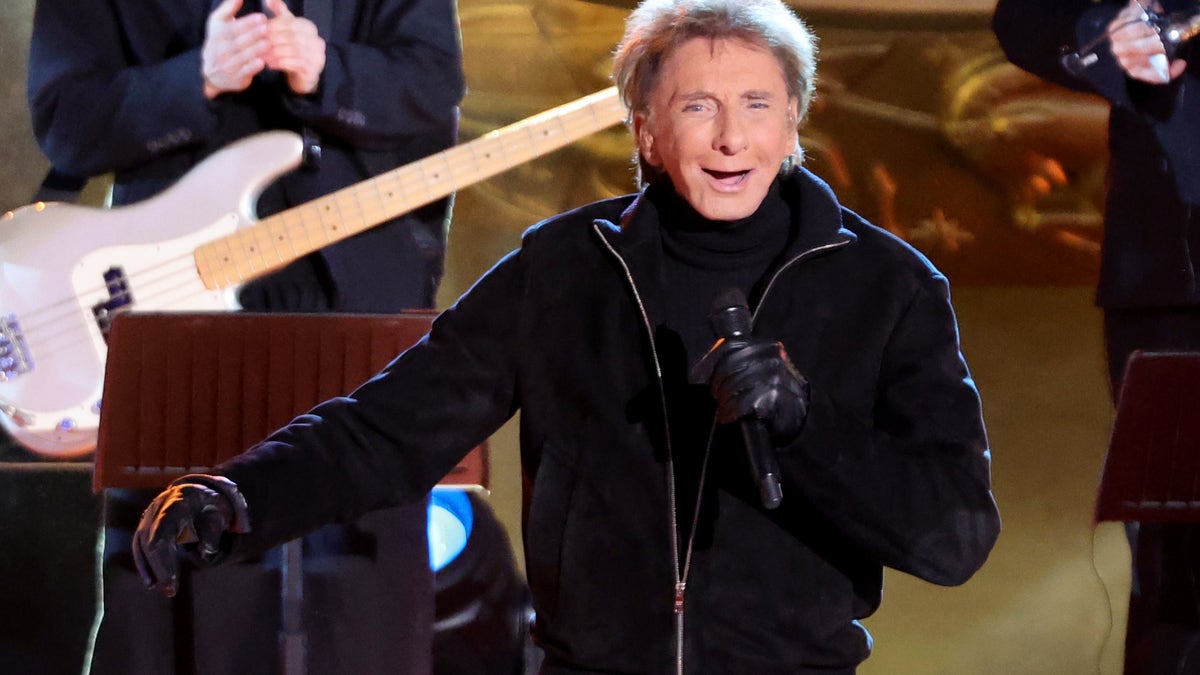 barry manilow holding a micriphone and smiling on stage