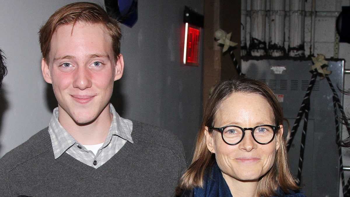 Charlie Foster in a grey sweater poses with his mother Jodie in circular glasses
