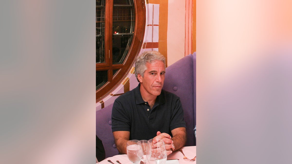 Jeffrey Epstein sitting at the dining table wearing a black polo shirt