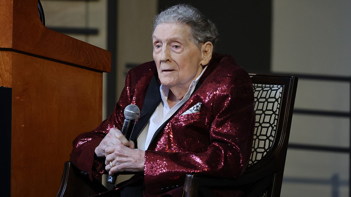 Jerry Lee Lewis holding a red sparkly blazer and holding a mic