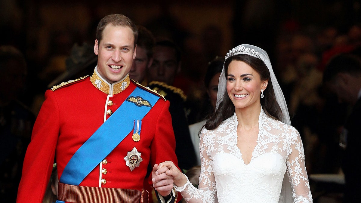 Prince Willim in a red suit and Kate Middleton in a bridal gown holding hands on their wedding day