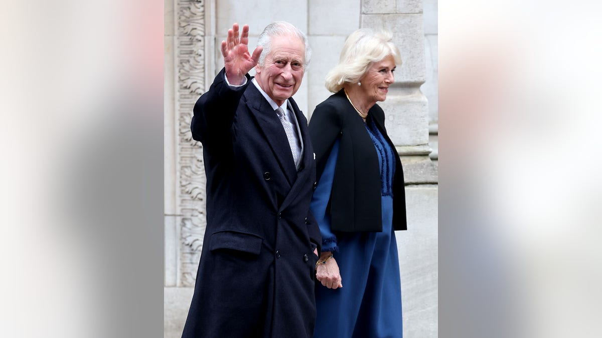 King Charles waving to the crowd next to Queen Camilla