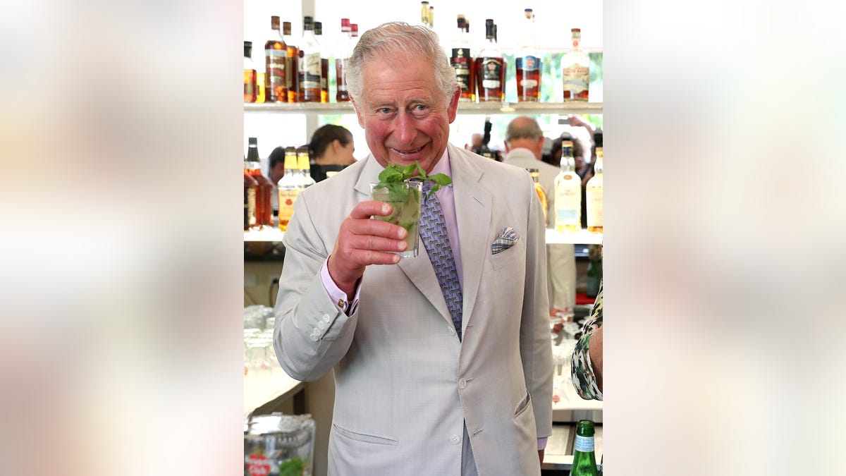 King Charles drinking a mojito while wearing an ivory suit and tie