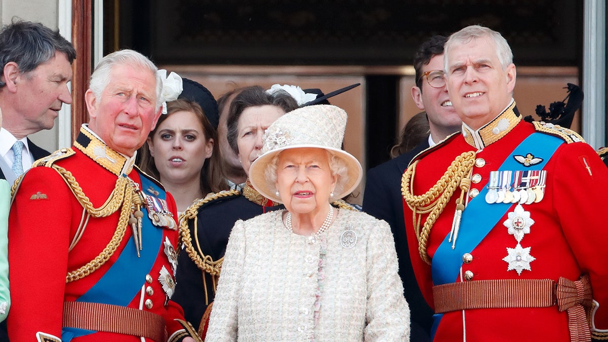 King Charles and Prince Andrew wearing matching red suits in between Queen Elizabeth on the Buckingham Palace balcony