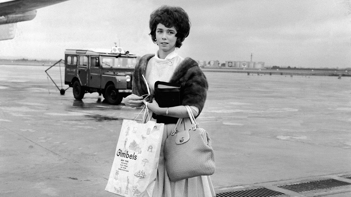 Myra Williams holding various bags as she steps out of an airplane