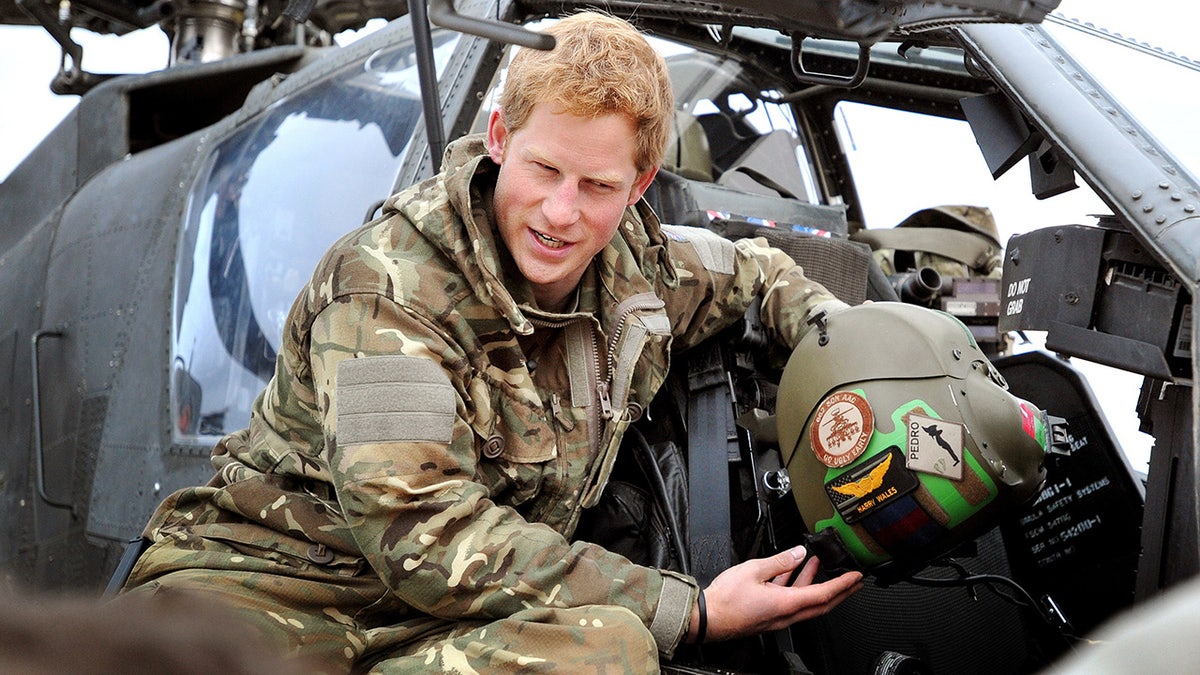 Príncipe Harry em traje militar na frente de um helicóptero