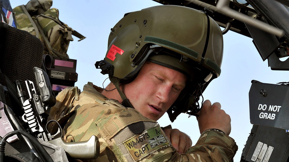 A close-up of Prince Harry in military uniform and a helmet inside a helicopter