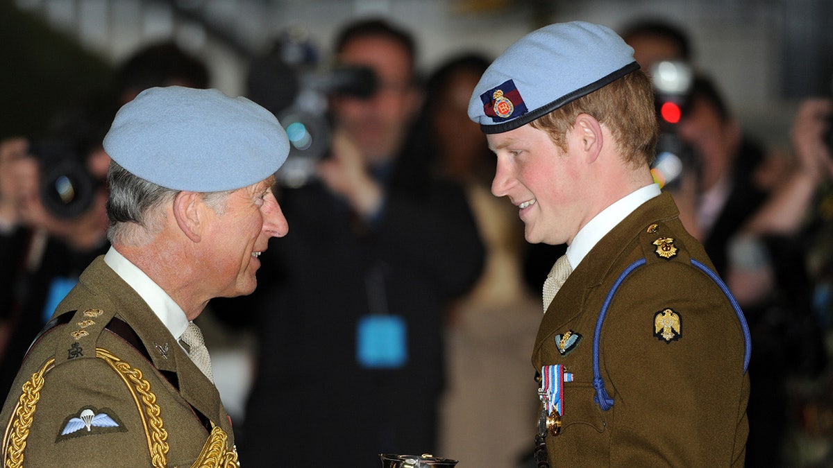 Prince Charles smiling at Prince Harry as they both wear uniforms