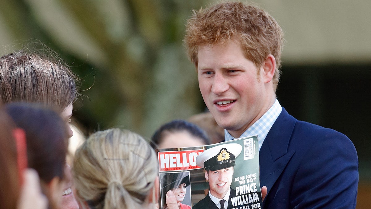 Prince Harry looking disgusted as he holds a magazine cover of his brother Prince William