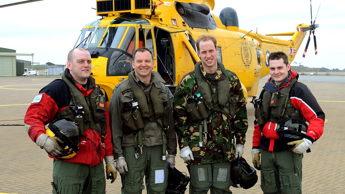 Prince William in front of a yellow helicopter with his crew