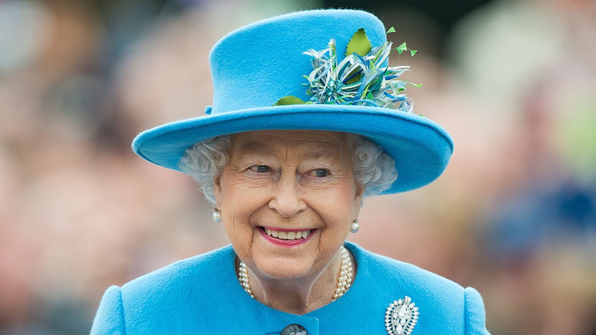 A close-up of Queen Elizabeth smiling in a blue coat dress and matching hat