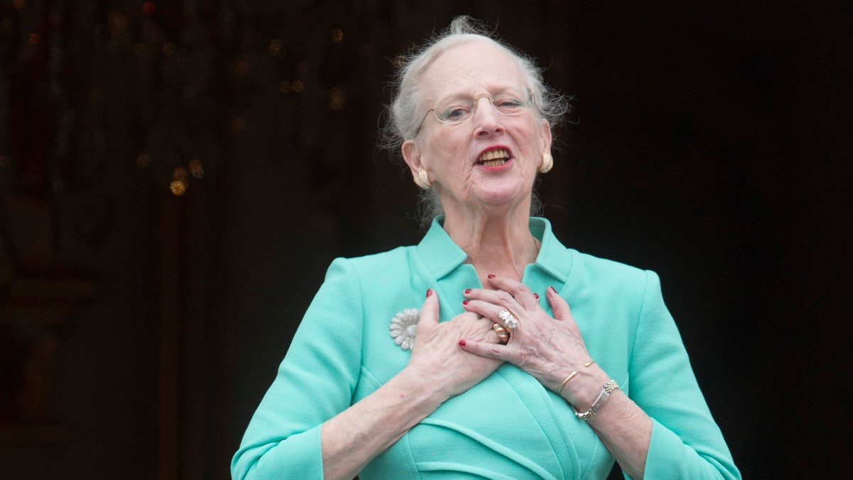 Queen Margrethe holding her chest and wearing an aqua blouse