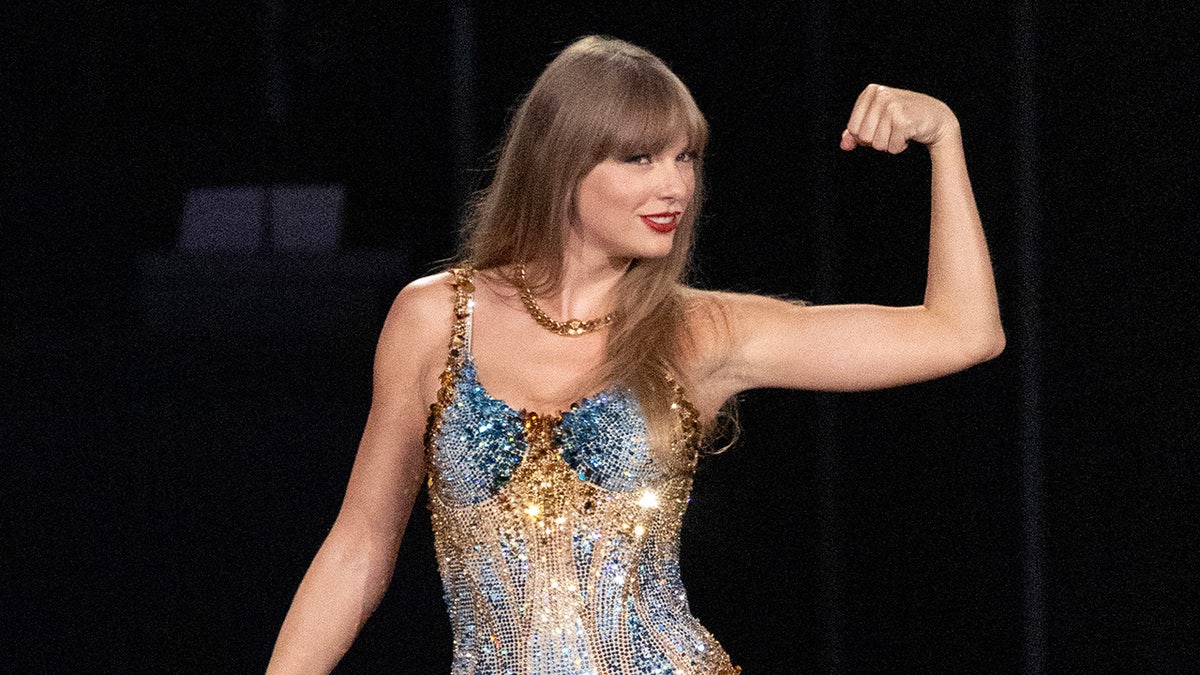 Taylor Swift smiling with her fist up wearing a sparkling bodysuit