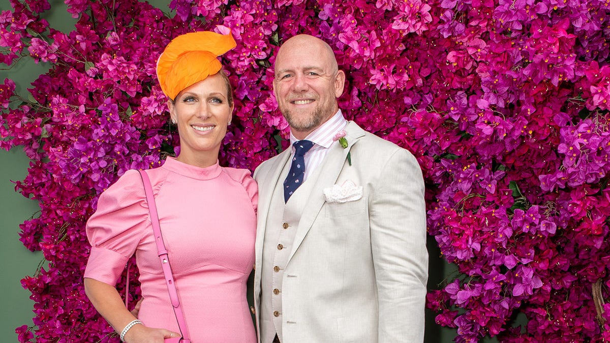 Zara Tindall wearing a pink dress and orange fascinator next to Mike Tindall in a beige suit