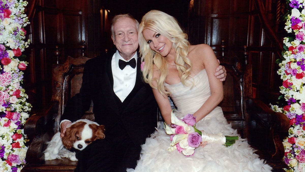 Crystal Hefner wearing a bridal gowl holding flowers next to Hugh Hefner in a suit and bowtie