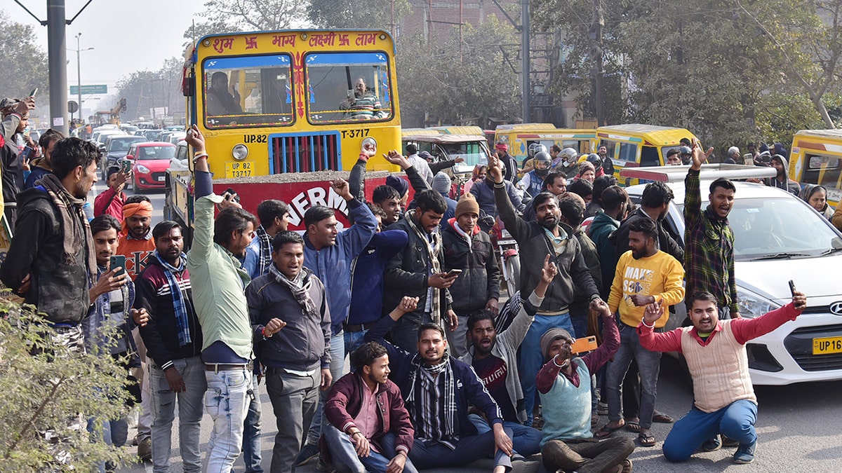 Male Indian protestors sit and stand in front of a bus on the road, protesting over new hit-and-run law