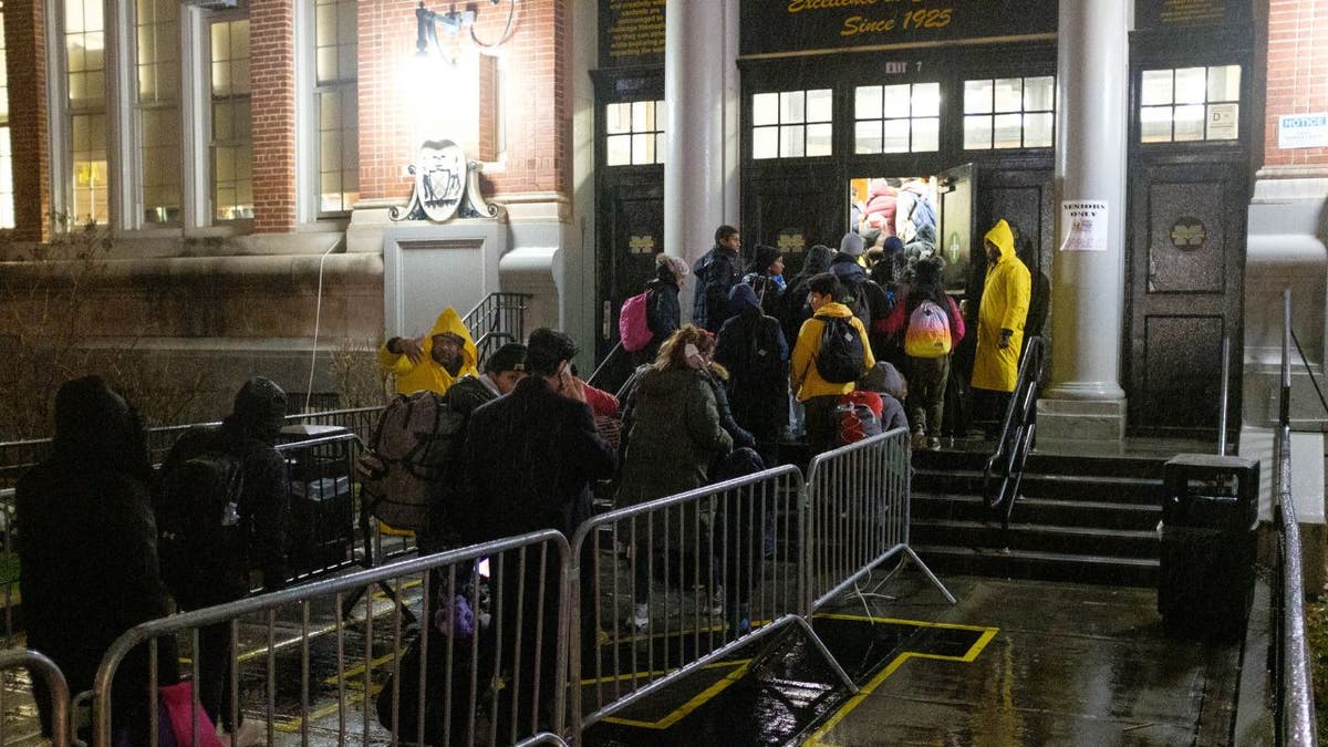 Migrants arrive in the rain at the front door of a Brooklyn school
