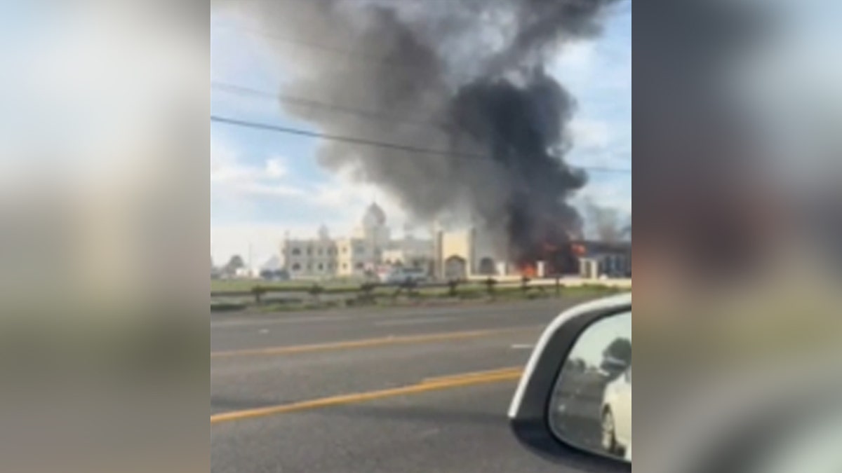 Car drives by Sikh temple caught on fire, dark gray smoke in sky