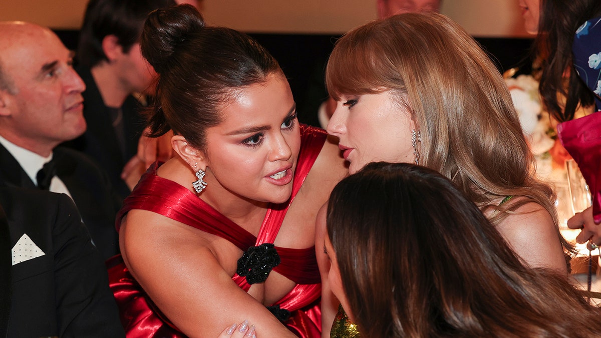 Selena Gomez se inclinando para falar com Taylor Swift