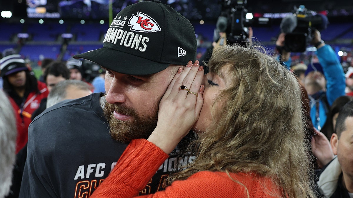 Taylor Swift covers her mouth as she talks to Travis Kelce