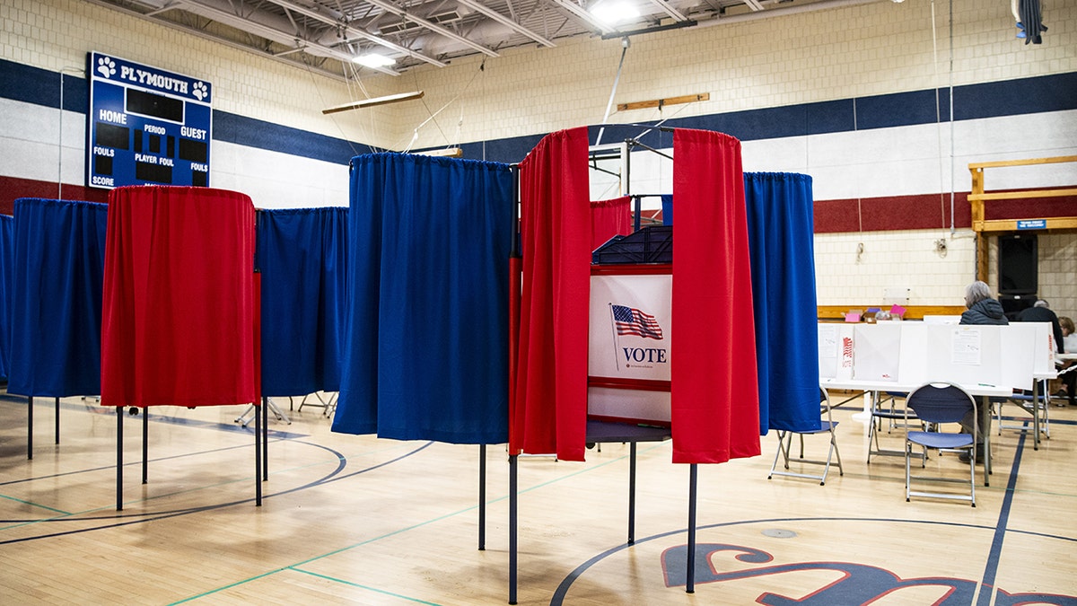 Voting booth in an elementary school gym, red and blue curtains, American flag with word VOTE on sign