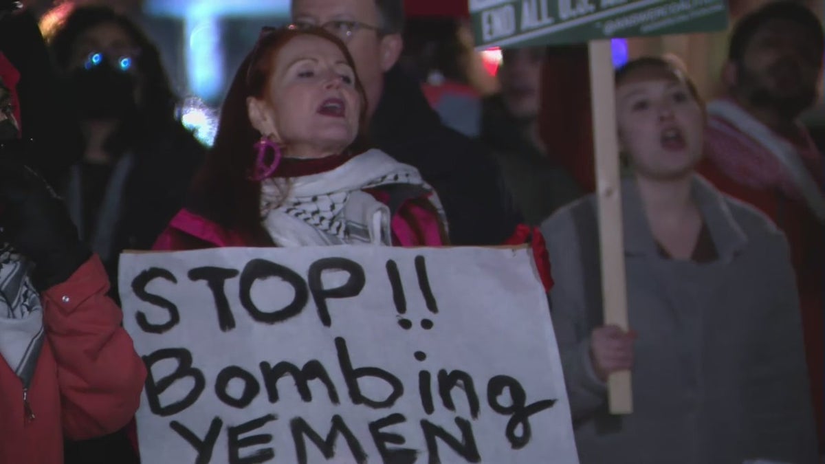 A protester holds a sign that says, "Stop!! Bombing Yemen"