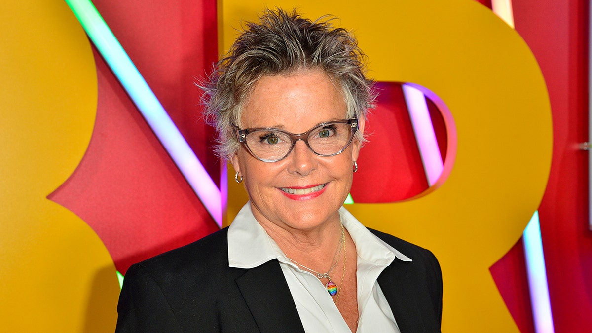 Amanda Bearse with grey and white spiky hair wearing a black suit and white top