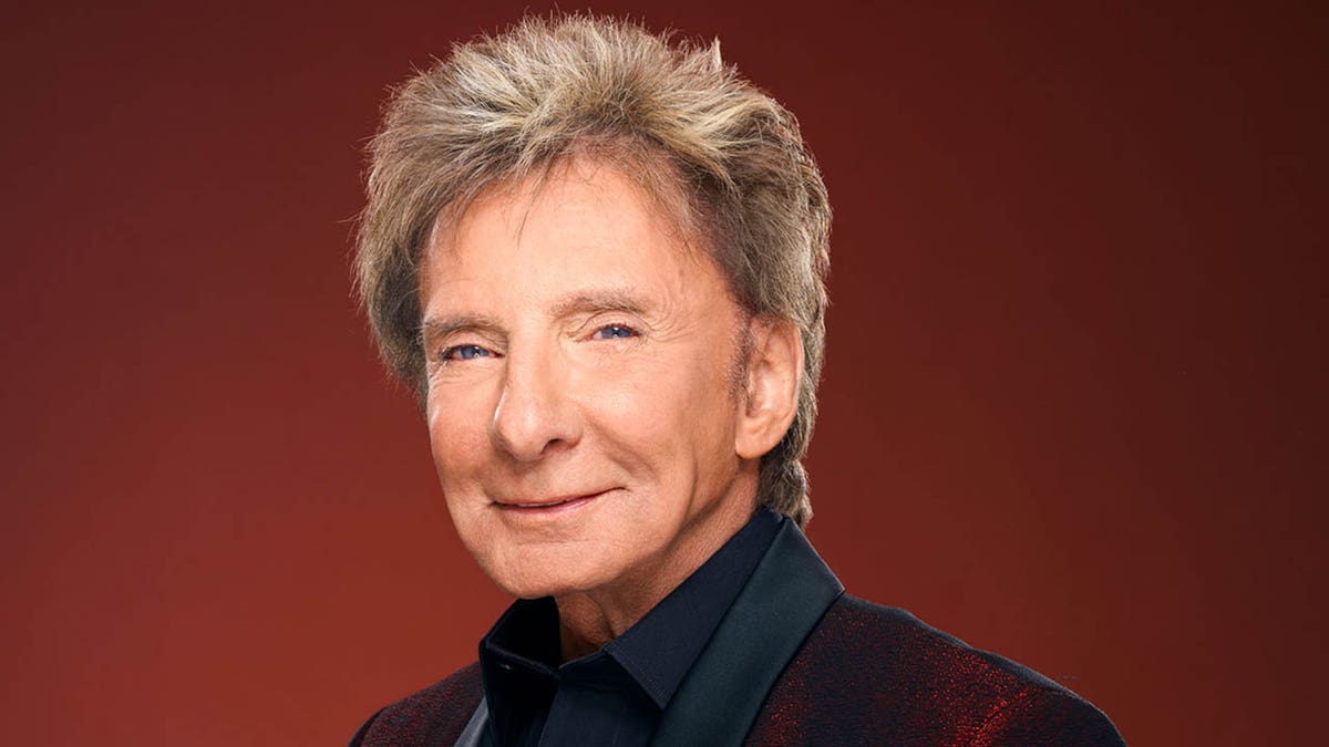barry manilow looking at the camera against a red backdrop