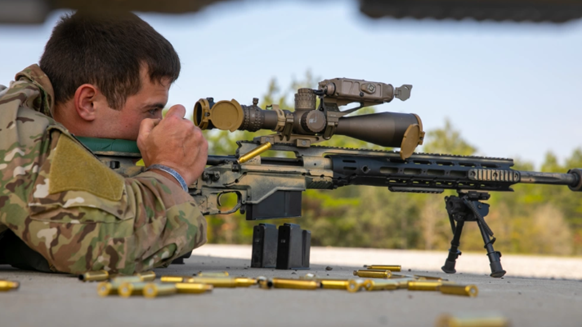 Army soldier looks through scope of sniper rifle