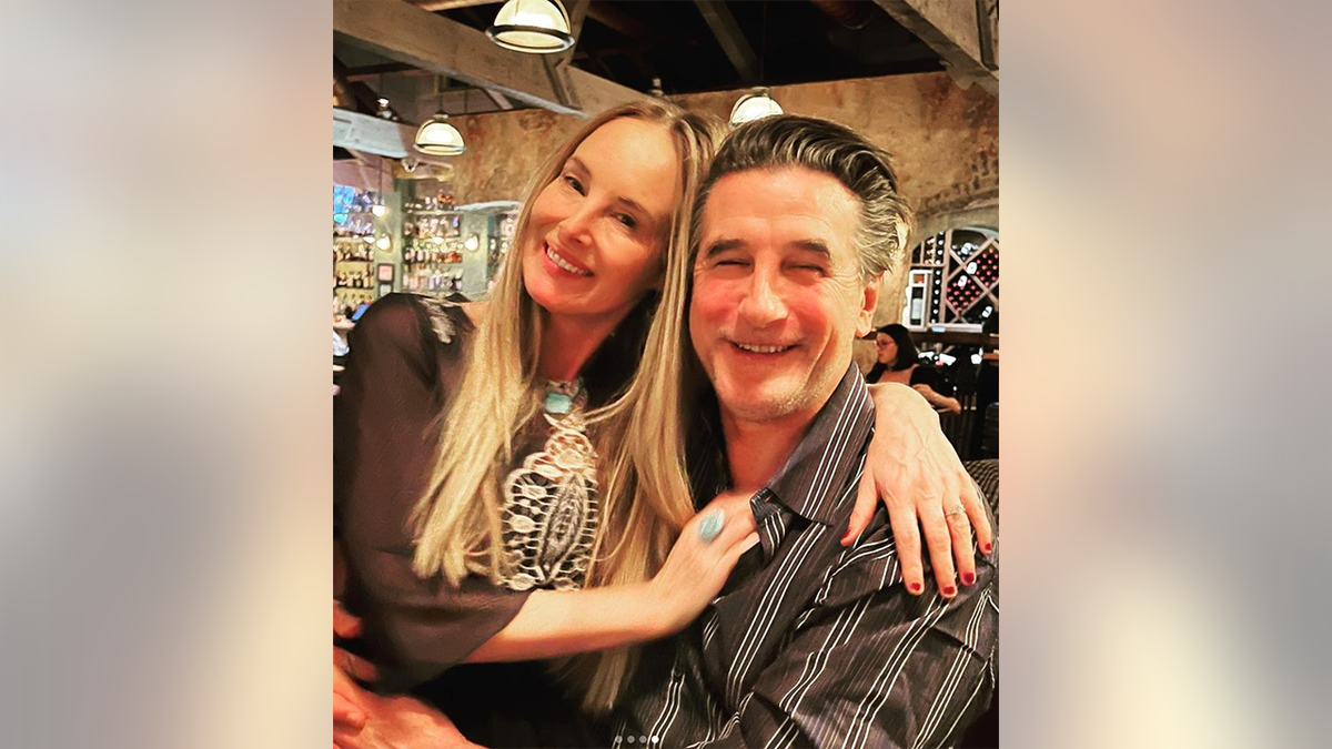 Billy Baldwin in a striped shirt hugs wife Chynna Philliips as they sit down