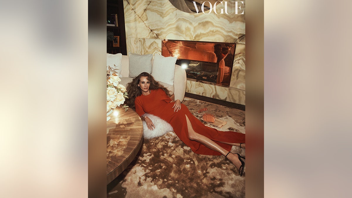 Julia Roberts in a dark orange dress with a slit lies on the floor against a couch in a picture for British Vogue