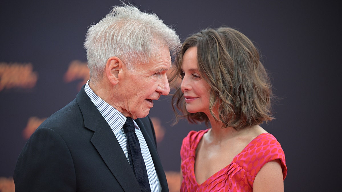 Calista Flockhart in a red dress looks lovingly and closely at husband Harrison Ford