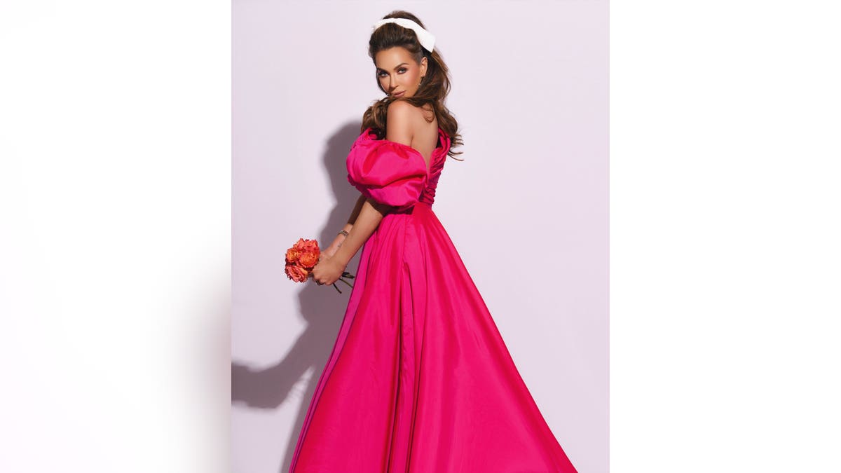 courtney sixx in a pink gown turned to the side holding bouquet